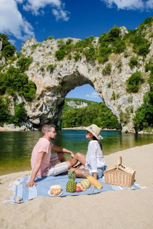 Photo for Couple having picnic on the beach on vacation in the Ardeche France Pont d Arc, Ardeche France, view of Natural arch in Vallon Pont dArc in Ardeche canyon in France Europe Rhone Alps Dordogne - Royalty Free Image