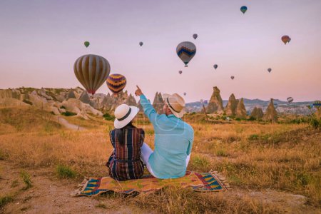 Photo for Cappadocia Turkey during sunrise, couple mid age men and woman on vacation in the hills of Goreme Capadocia Turkey, men and woman looking sunrsise with hot air balloons in Cappadocia Turkey - Royalty Free Image