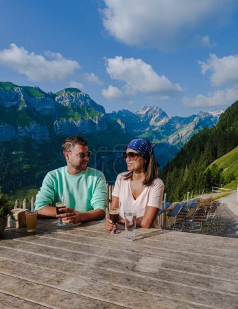 Photo for A couple of men and women drinking coffee at Berggasthaus Aescher in den Appenzeller Alpen at sunset, a restaurant under a cliff on mountain Ebenalp in Switzerland, Appenzell - Royalty Free Image