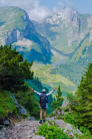 Téléchargez les photos : Femmes asiatiques avec les mains en l'air randonnée dans les Alpes suisses pendant les vacances d'été avec un sac à dos et des bottes de randonnée. femme marchant sur le sentier Saxer Lucke - en image libre de droit