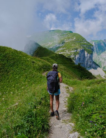 Téléchargez les photos : Femmes asiatiques marchant dans les Alpes suisses pendant les vacances d'été avec un sac à dos et des bottes de randonnée. femme marchant sur le sentier Saxer Lucke - en image libre de droit