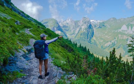 Téléchargez les photos : Femmes asiatiques avec les mains en l'air randonnée dans les Alpes suisses pendant les vacances d'été avec un sac à dos et des bottes de randonnée. femme marchant sur le sentier Saxer Lucke - en image libre de droit