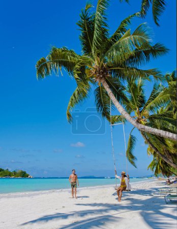 Praslin Seychelles tropical island with white beaches and palm trees, a couple of men and women in hammocks swing on the beach under a palm tree at Anse Volber Seychelles.