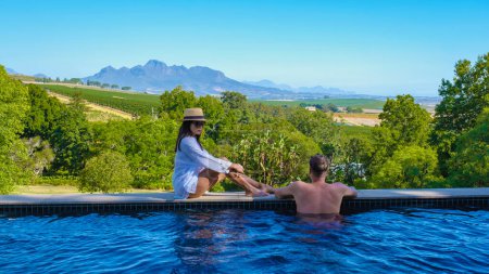 Téléchargez les photos : Couple d'hommes et de femmes dans une piscine donnant sur les vignobles et les montagnes de Stellenbosch Afrique du Sud. - en image libre de droit