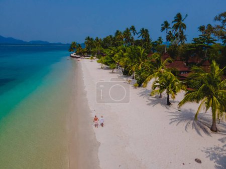 Foto de Un par de hombres y mujeres de vacaciones en la isla tropical de Koh Mook en el mar de Andamán en Tailandia, hombres y mujeres caminando en una playa con palmeras vista aérea de drones - Imagen libre de derechos