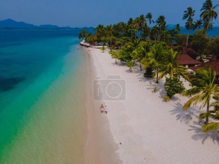 Téléchargez les photos : Un couple d'hommes et de femmes en vacances à Koh Mook île tropicale dans la mer d'Andaman en Thaïlande, hommes et femmes marchant sur une plage avec des palmiers par une journée ensoleillée - en image libre de droit