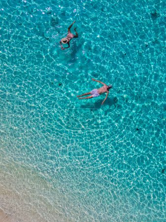 Photo for A couple swimming in the ocean of Koh Kradan Island with a white tropical beach and turqouse colored ocean. men and women in a blue ocean seen from above with a drone on a sunny day - Royalty Free Image