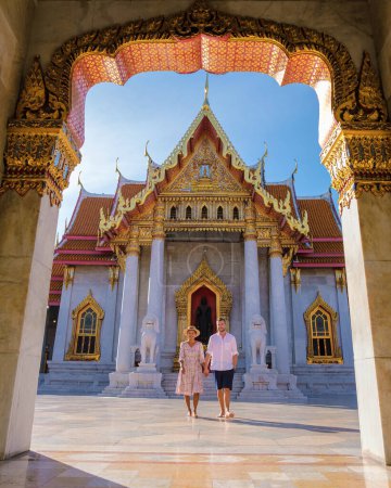 Téléchargez les photos : Un couple d'hommes et de femmes visitent le temple Wat Benchamabophit à Bangkok en Thaïlande, le temple du marbre à Bangkok. Femme asiatique avec un chapeau et les hommes européens visitant un temple à Bangkok - en image libre de droit