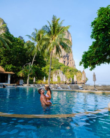 Foto de Pareja de hombres y mujeres en una piscina en un complejo de lujo en Tailandia. Piscina de lujo con sillas y sombrillas en Railay Beach Krabi - Imagen libre de derechos