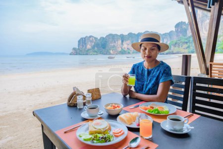 Téléchargez les photos : Femme prenant le petit déjeuner sur la plage, Petit déjeuner dans un hôtel de luxe sur la plage de Railay Krabi Thaïlande. - en image libre de droit