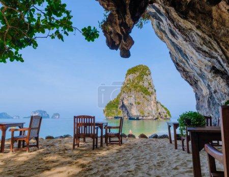 Téléchargez les photos : Restaurant avec chaises longues sur la plage à une grotte de falaise calcaire à Railai Beach Krabi Thaïlande par une journée ensoleillée à la plage de Phrangna - en image libre de droit