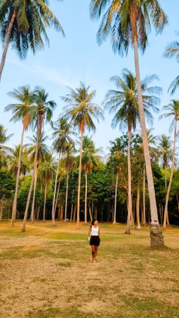 Photo for Women walking under palm trees Palm trees with a blue sky and clouds in Koh Lanta Thailand. Green palm trees in the sky during sunset at a tropical Island - Royalty Free Image