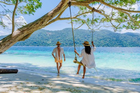 Couple playing at a rope swing on the beach of Ko Ra Wi Island Southern Thailand, tropical white sandy beach with turqouse colored ocean at Tarutao National Park, Koh Rawi, Tambon Ko Tarutao