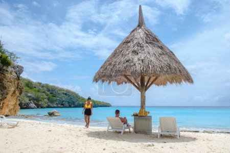A couple of men and women on vacation in Curacao, Cas Abao Beach Playa Cas Abao Caribbean island of Curacao, Playa Cas Abao tropical white beach with beach chairs and a tatched beach umbrella 