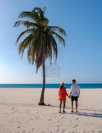 Téléchargez les photos : Palm Beach Aruba Caribbean, un couple d'hommes et de femmes sur une longue plage de sable blanc avec des palmiers aux Antilles Aruba pendant les vacances - en image libre de droit