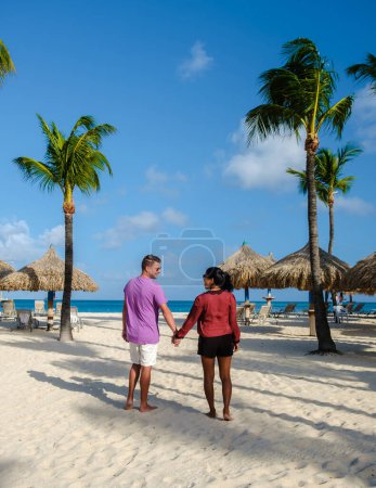 Téléchargez les photos : Palm Beach Aruba Caribbean, un couple d'hommes et de femmes sur une longue plage de sable blanc avec des palmiers aux Antilles Aruba. - en image libre de droit