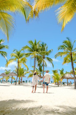 Foto de Palm Beach Aruba Caribbean, un par de hombres y mujeres en una larga playa de arena blanca con palmeras en las Antillas de Aruba. - Imagen libre de derechos
