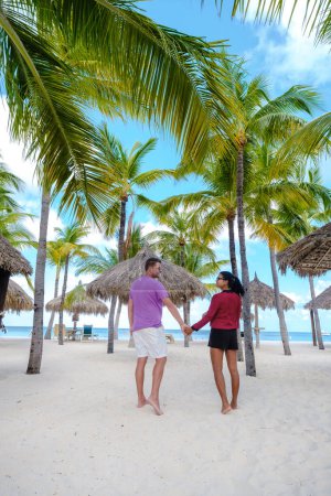Téléchargez les photos : Palm Beach Aruba Caribbean, un couple d'hommes et de femmes sur une longue plage de sable blanc avec des palmiers aux Antilles Aruba. - en image libre de droit