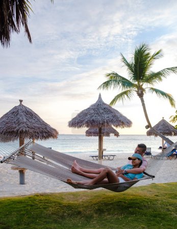 Foto de Palm Beach Aruba Caribbean, un par de hombres y mujeres en una hamaca en una larga playa de arena blanca con palmeras en las Antillas de Aruba. - Imagen libre de derechos