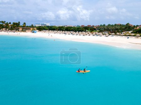Photo for Couple Kayaking in the Ocean on Vacation Aruba Caribbean Sea, man and woman mid age kayak in ocean blue clear water with white beach and palm trees Aruba - Royalty Free Image