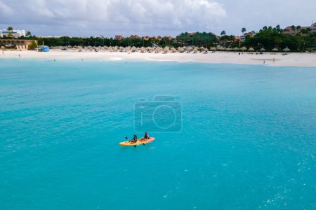 Photo for Couple Kayaking in the Ocean on Vacation Aruba Caribbean Sea, man and woman mid age kayak in ocean blue clear water with white beach and palm trees Aruba Island - Royalty Free Image