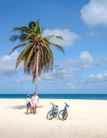 Téléchargez les photos : Eagle Beach Aruba, Palmiers sur le rivage d'Eagle Beach à Aruba, quelques hommes, et une femme sur la plage d'Aruba avec un vélo - en image libre de droit