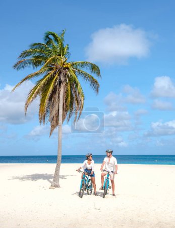 Foto de Eagle Beach Aruba, Palmeras en la costa de Eagle Beach en Aruba, un par de hombres, y una mujer en la playa de Aruba con una bicicleta - Imagen libre de derechos