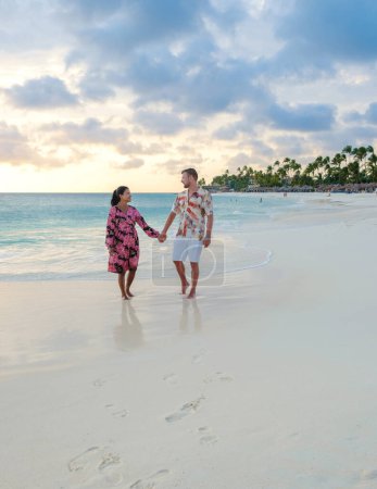 Foto de Palm Beach Aruba Caribbean, un par de hombres y mujeres en una larga playa de arena blanca con palmeras en las Antillas de Aruba con un océano de color turquesa - Imagen libre de derechos