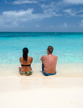 Téléchargez les photos : Palm Beach Aruba Caribbean, un couple d'hommes et de femmes sur une longue plage de sable blanc avec des palmiers aux Antilles d'Aruba avec un océan de couleur turque - en image libre de droit