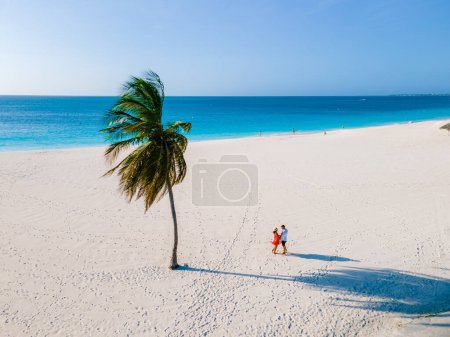 Téléchargez les photos : Palmiers sur le rivage d'Eagle Beach à Aruba, un couple d'hommes et de femmes sur la plage d'Aruba - en image libre de droit