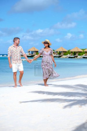 Photo for Couple of men and women on vacation at Aruba Island Caribbean walking on a tropical white beach with turqouse colored ocean and palm trees with overwater bungalows at a luxury resort. - Royalty Free Image