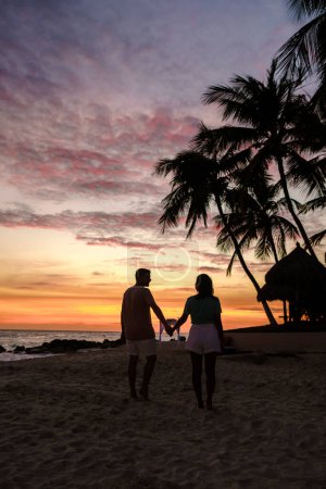 Téléchargez les photos : Quelques hommes et femmes sont sur la plage à regarder le coucher du soleil pendant les vacances à Aruba Island Caribbean. homme et femme au bord de l'océan pendant le susnet - en image libre de droit