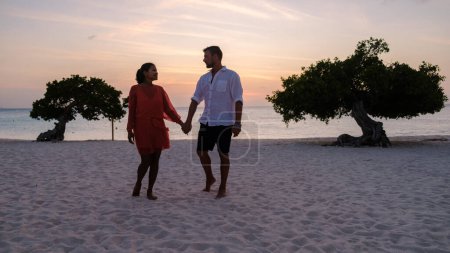 Photo for Divi Divi Trees on the shoreline of Eagle Beach in Aruba, a couple of men, and a woman on the beach of Aruba during sunset - Royalty Free Image