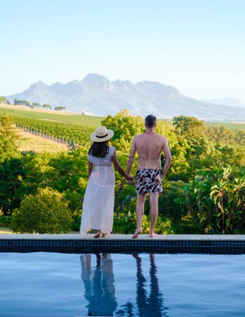 Téléchargez les photos : Couple d'hommes et de femmes dans un paysage viticole au coucher du soleil avec des montagnes à Stellenbosch, près de Cape Town, Afrique du Sud. raisin sur la vigne dans le vignoble Western Cape Afrique du Sud - en image libre de droit