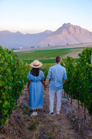 Foto de Pareja de hombres y mujeres en un paisaje de viñedo al atardecer con montañas en Stellenbosch, cerca de Ciudad del Cabo, Sudáfrica. uvas de vino en la vid en el viñedo Western Cape Sudáfrica - Imagen libre de derechos