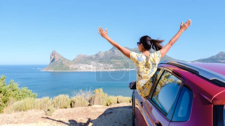 Photo for Woman outside a car window with hands up, a car at Chapmans Peak Drive in Cape Town South Africa looking out over the ocean. women on a road trip garden route South Africa with renal car - Royalty Free Image
