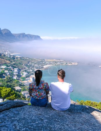 Foto de Un par de hombres y mujeres en el mirador de The Rock en Ciudad del Cabo sobre Campsbay, vista sobre Camps Bay con niebla sobre el océano. niebla procedente del océano en Camps Bay Cape Town Sudáfrica - Imagen libre de derechos