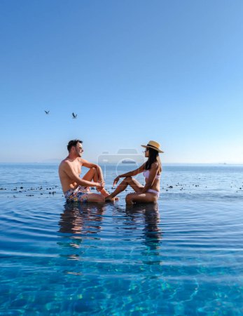 Téléchargez les photos : Couple homme et femme d'âge moyen devant la piscine Infinity donnant sur l'océan du Cap en Afrique du Sud, homme et femme dans une piscine pendant le coucher du soleil. - en image libre de droit
