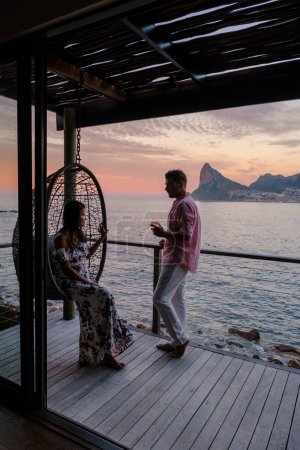 Téléchargez les photos : Couple homme et femmes regardant le coucher du soleil sur le balcon en vacances au Cap Afrique du Sud. - en image libre de droit