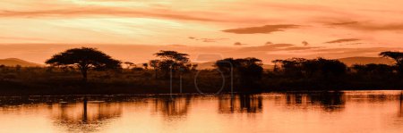 Photo for Sunset by a water pool lake in the Savannah of South Africa KwaZulu Natal. beautiful sunset by the lake in South Africa during a safari with trees and mountains on the background - Royalty Free Image