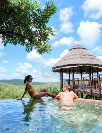 Téléchargez les photos : Couple hommes et femmes au bord de la piscine lors d'un safari de luxe, Afrique du Sud, un lodge de safari de luxe dans la brousse d'une réserve de gibier - en image libre de droit
