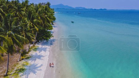 Ein paar Männer und Frauen im Urlaub auf der tropischen Insel Koh Mook in der Andamanensee in Thailand, Männer und Frauen spazieren an einem Strand mit Palmen
