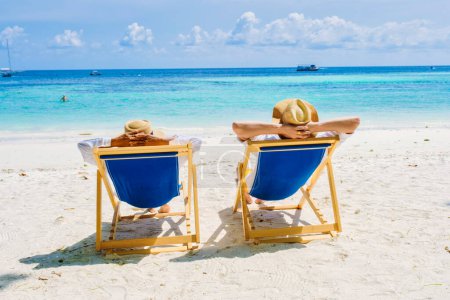 Téléchargez les photos : Un couple d'hommes et de femmes sur des chaises longues sur la plage de l'île de Koh Lipe, au sud de la Thaïlande, avec un océan de couleur turque et une plage de sable blanc à Ko Lipe. - en image libre de droit