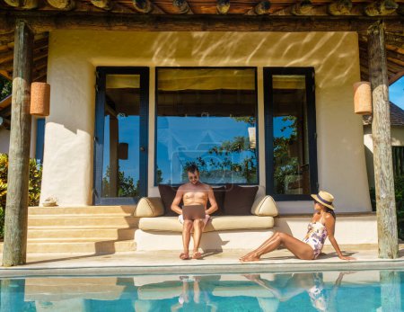 Foto de Hombres y mujeres nómadas digitales de trabajo en línea remotos y portátil sentado en una piscina de agua turquesa soleada en una villa de piscina privada, hombre de negocios con maqueta - Imagen libre de derechos