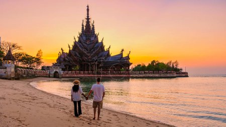 Photo for A couple of men and women visit the Sanctuary of Truth, Pattaya, Thailand, wooden temple by the ocean during sunset on the beach of Pattaya. - Royalty Free Image