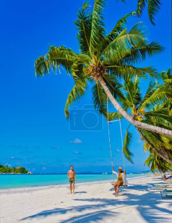 Téléchargez les photos : Praslin Seychelles île tropicale avec des plages blanches et des palmiers, un couple d'hommes et de femmes dans des hamacs balancent sur la plage sous un palmier à Anse Volber Seychelles. - en image libre de droit