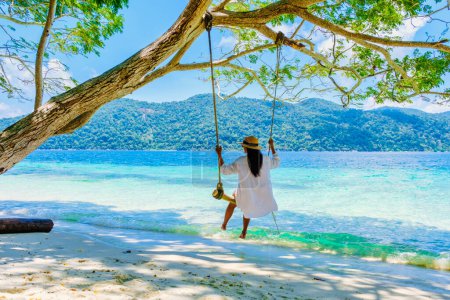 Téléchargez les photos : Femme se balançant sous un arbre à une balançoire sur la plage de Koh Lipe Island sud de la Thaïlande avec turqouse couleur océan et plage de sable blanc à Ko Lipe. Parc national de Tarutao, île de Koh Rawi - en image libre de droit