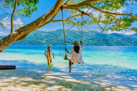 Téléchargez les photos : Un couple d'hommes et de femmes sont sur la plage avec une balançoire à corde à Koh Lipe Island sud de la Thaïlande avec turqouse couleur océan et plage de sable blanc à Ko Lipe. Parc national de Tarutao, île de Koh Rawi - en image libre de droit