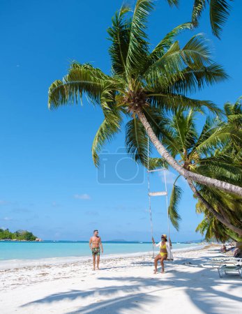 Téléchargez les photos : Un couple d'hommes et de femmes sur une plage tropicale avec une balançoire sous un palmier, île Anse Volbert Praslin aux Seychelles vue aérienne sur la plage Anse Volbert Cote dOr. - en image libre de droit