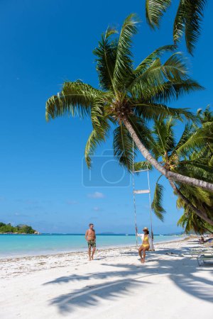 Photo for A couple of men and women on a tropical beach with a swing under a palm tree , Anse Volbert Praslin island in Seychelles aerial view on Anse Volbert Cote dOr beach. - Royalty Free Image